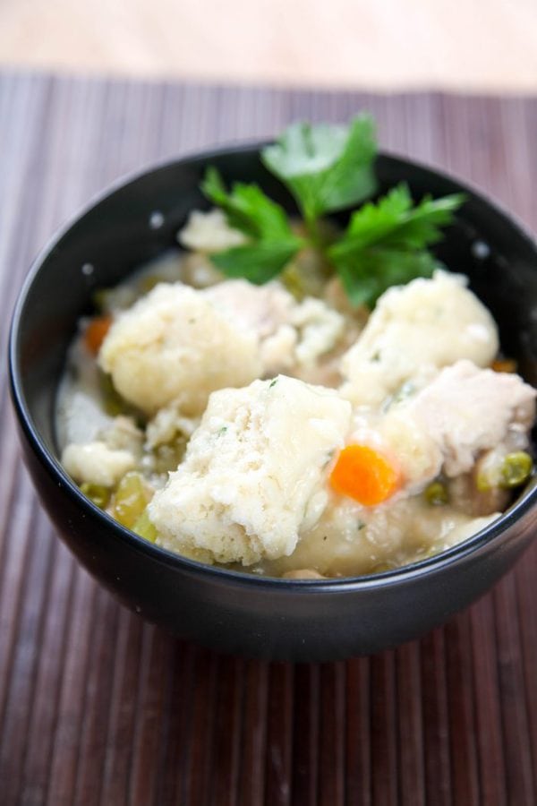 a black bowl filled with chicken and dumplings garnished with fresh parsley. 