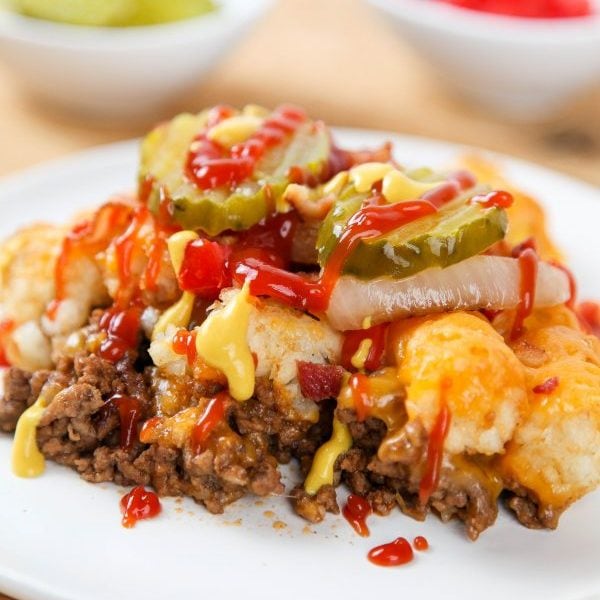 A ground beef tater tot casserole topped with ketchup, mustard, and pickles.