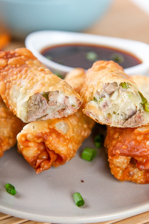 an steak egg roll cut if half and filled with steak, cheese, peppers and onions balancing on top of more egg rolls. 