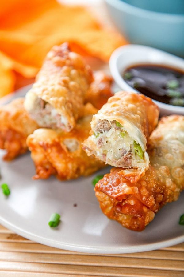 a plate of egg rolls filled with steak, peppers and cheese with one egg roll cut in half.