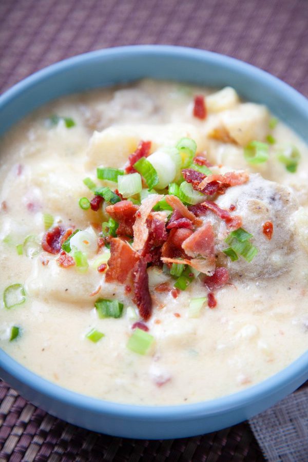 a blue bowl of potato sour garnished with bacon and green onions.