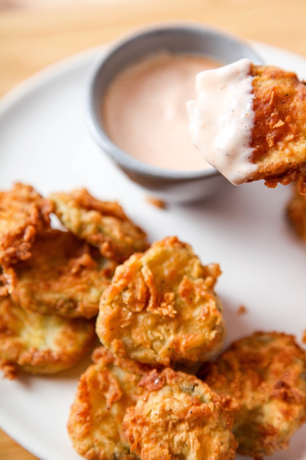 a breaded pickle being dipped into spicy ranch dressing. 