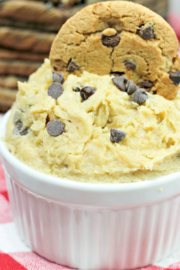 edible cookie dough in a white bowl with a chocolate chip cookie on top.