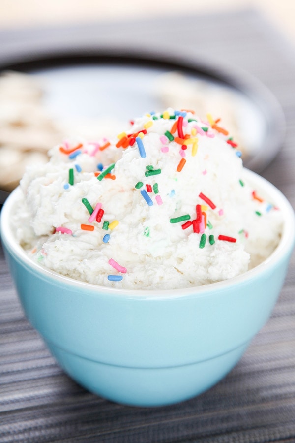 a blue bowl piled high with white dunkaroo dip and topped with rainbow sprinkles. 