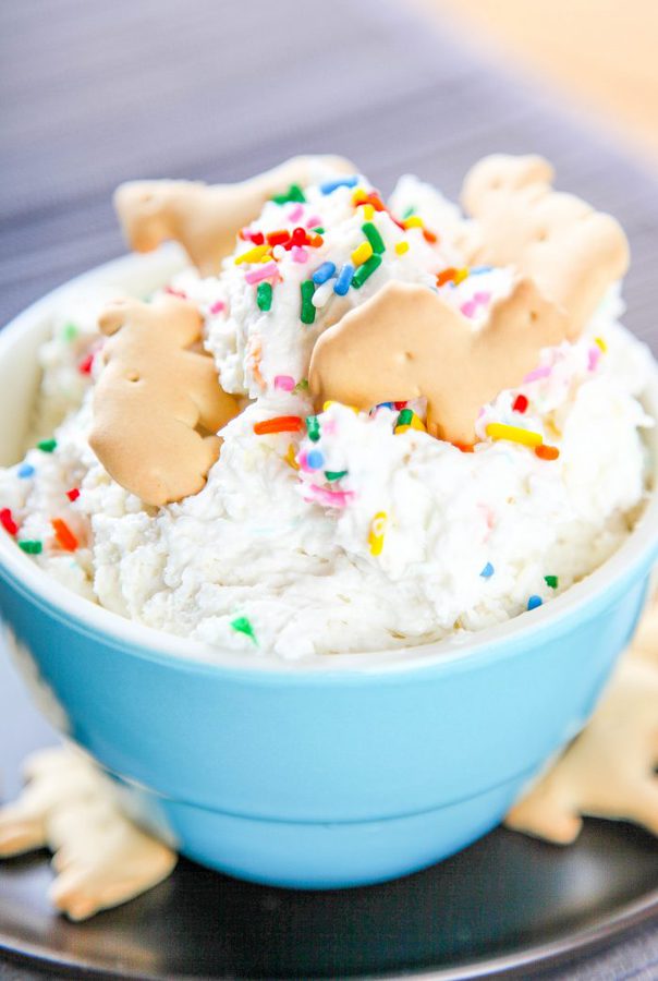 a blue bowl of funfetti dip topped with rainbow sprinkles and animal crackers.
