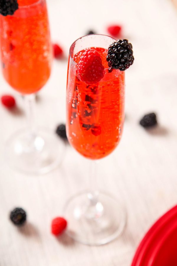 a bubbly red kir royale drink garnished with raspberries and blackberries. 
