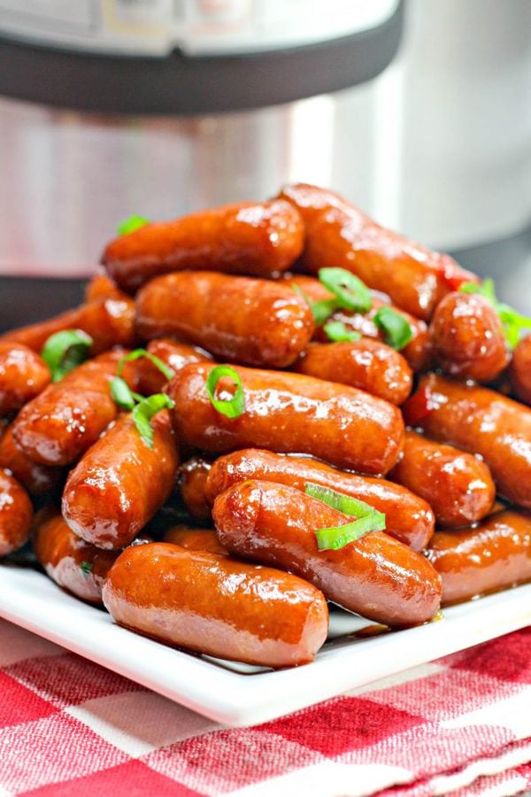 a tall pile of little smokie sausages in a sweet and tangy sauce garnished with green onions.