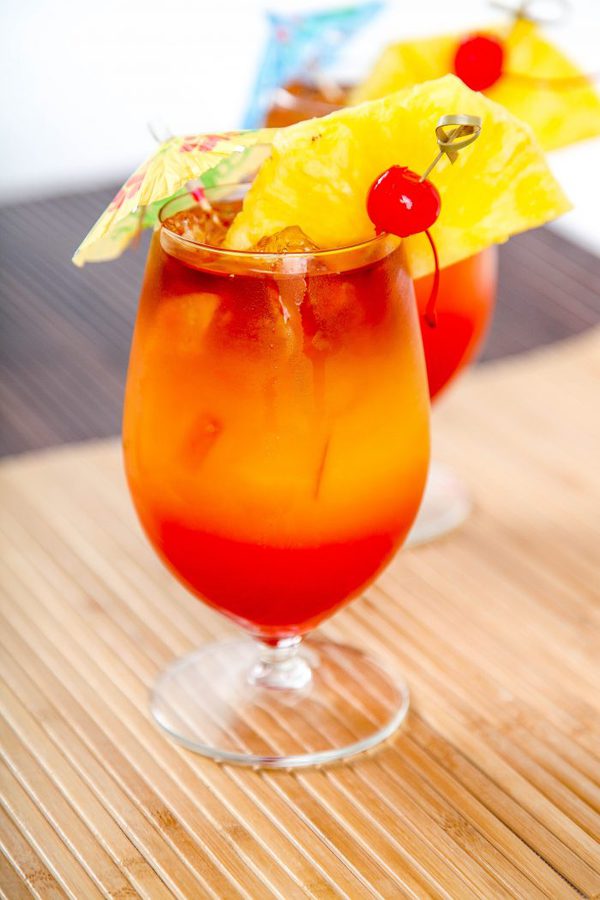 2 bahama mamas drinks made with rum, juice, and grenadine and garnished with pineapple.