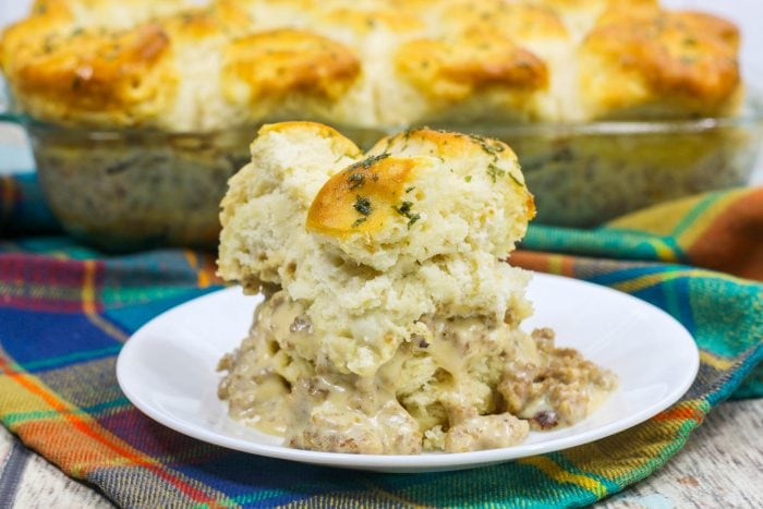 a white plate with layers of biscuits and sausage gravy on a rainbow tea towel. 