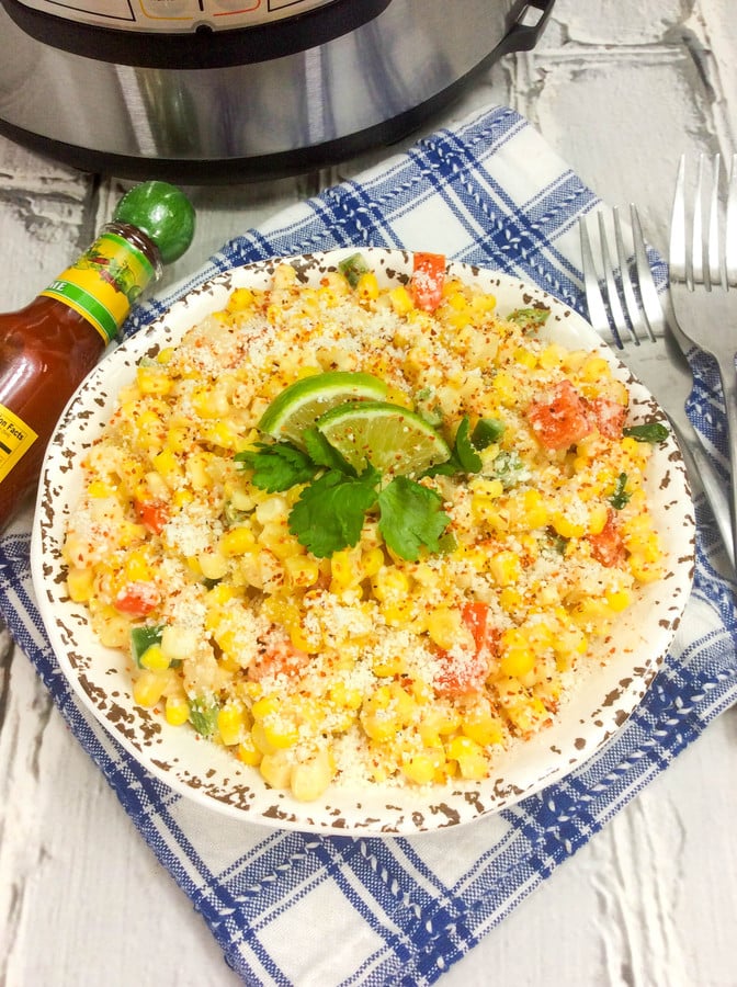 mexican street corn salad in a white bowl with an instant pot and a bottle of hot sauce in the background.