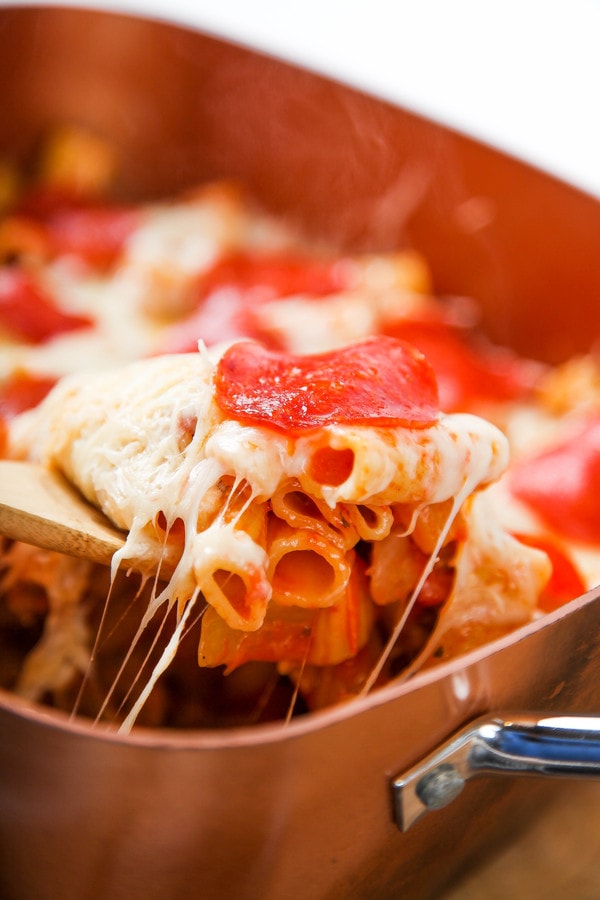 a wooden spoon lifting out pizza pasta topped with mozzarella cheese and pepperoni.