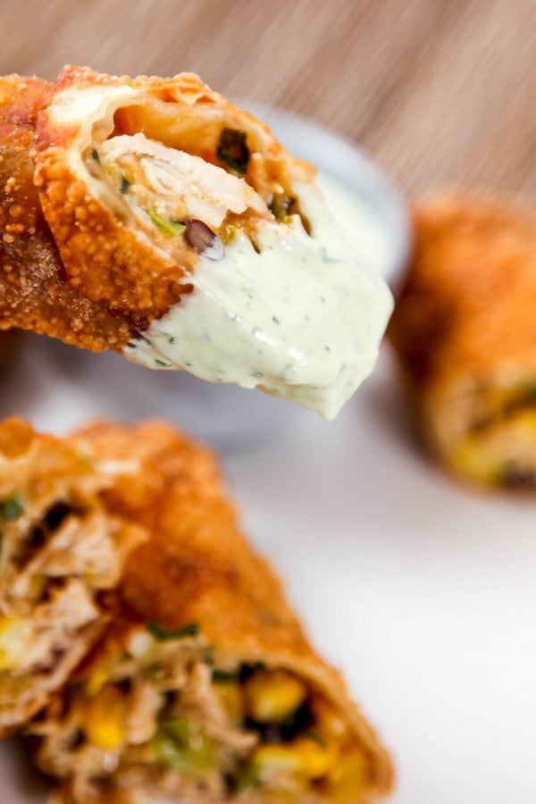 a closeup image of a southwestern egg roll with a bite out of it being dipped in avocado ranch. 