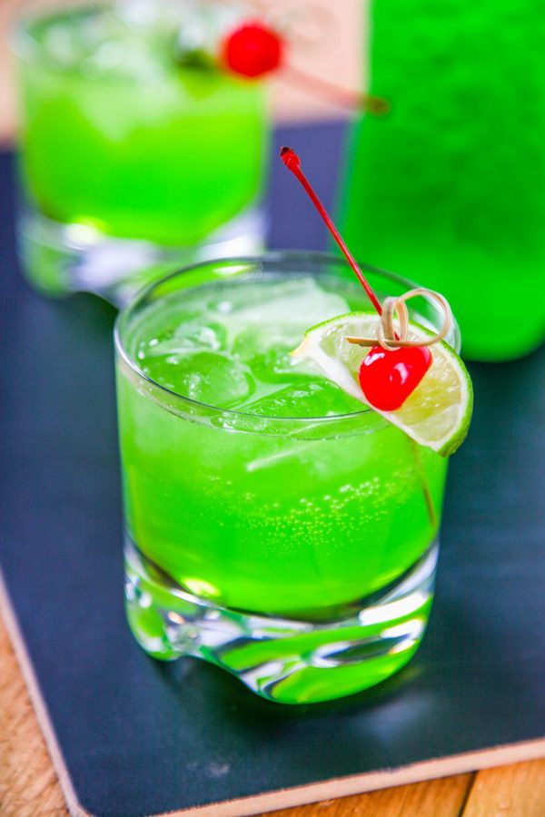a bright green midori drink filled with ice and garnished with a lime and a cherry.