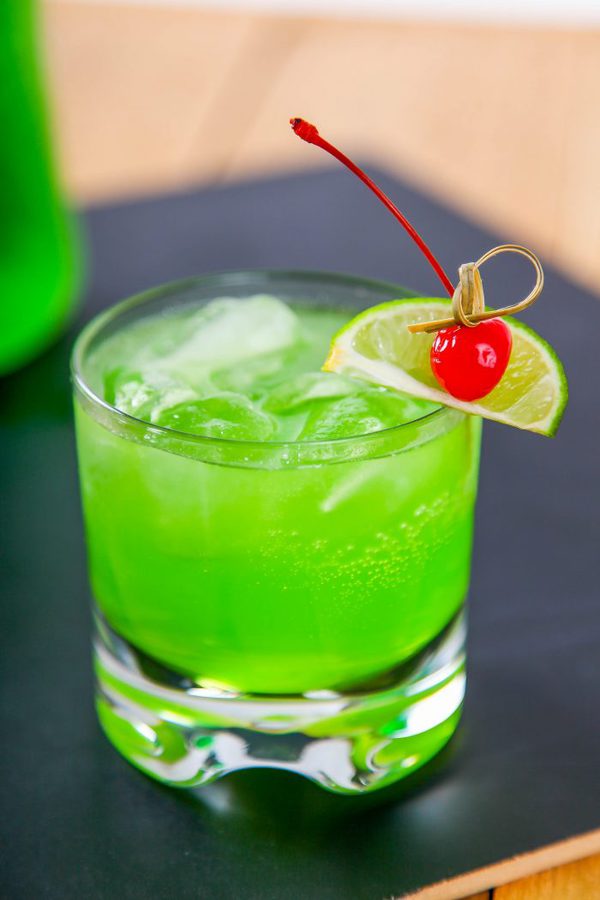 a midori sour cocktail garnished with a slice of lime and a maraschino cherry.