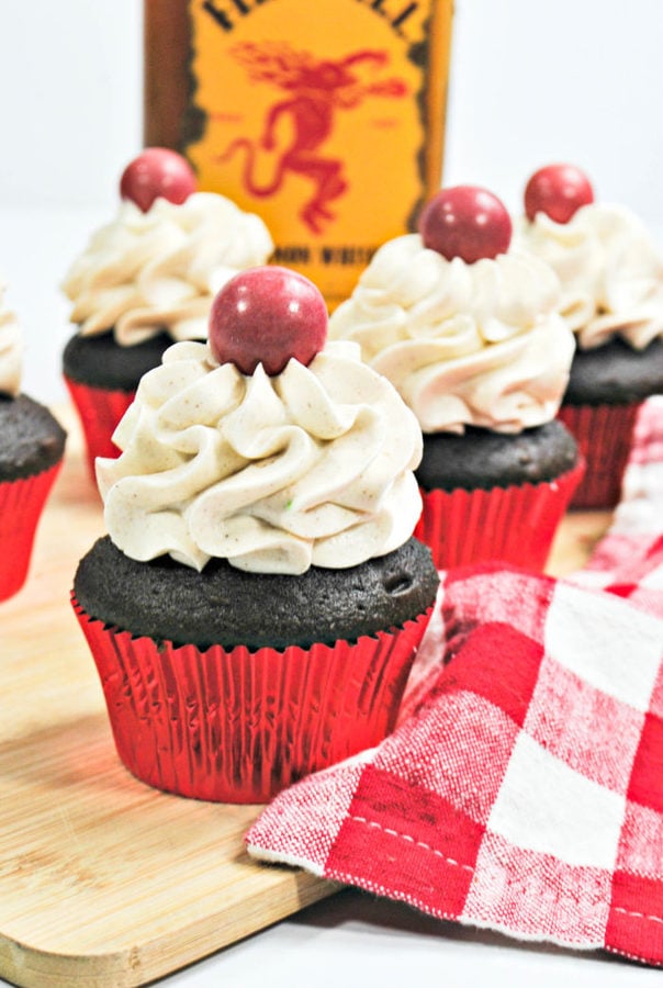 chocolate fireball cupcakes topped with a fireball candy with a bottle of Fireball in the background.