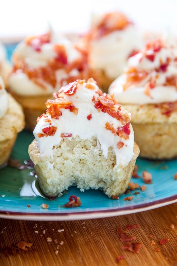 a maple cupcake with a bite taken out of it topped with maple buttercream and crumbled bacon.