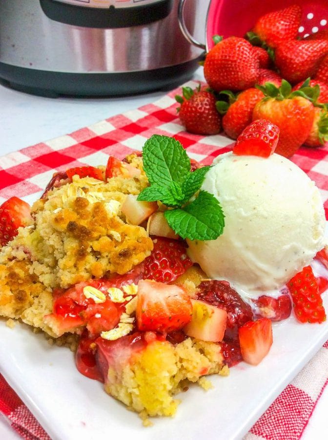 a white plate with strawberry dump cake topped with vanilla ice cream and fresh mint.