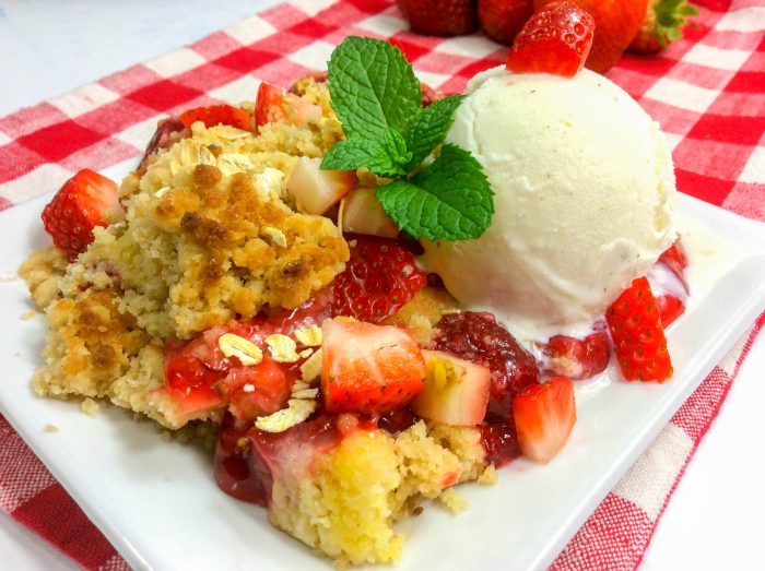 a closeup of a strawberry dump cake topped with more strawberries, ice cream, and mint.