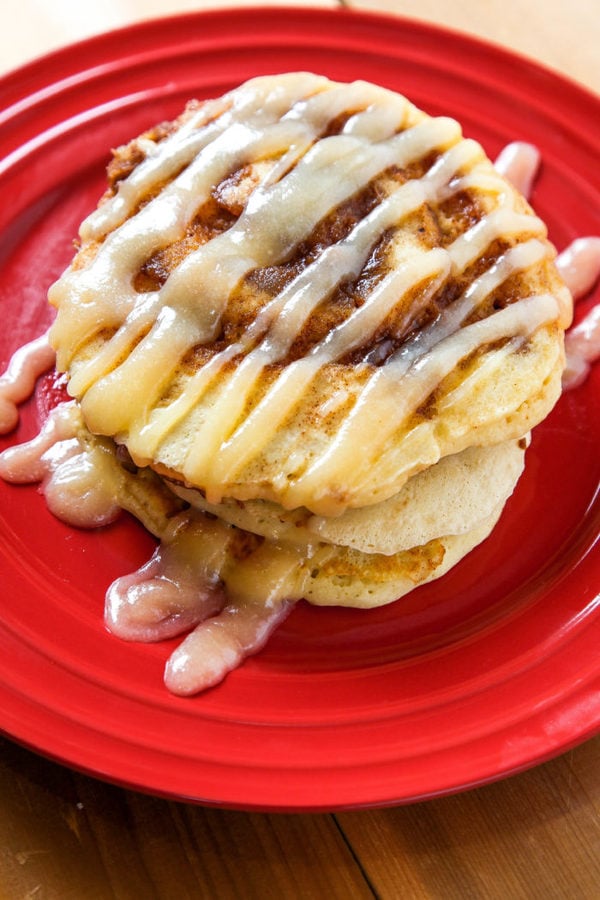 an overhead shot of cinnamon swirl pancakes with cream cheese drizzle on a red plate. 