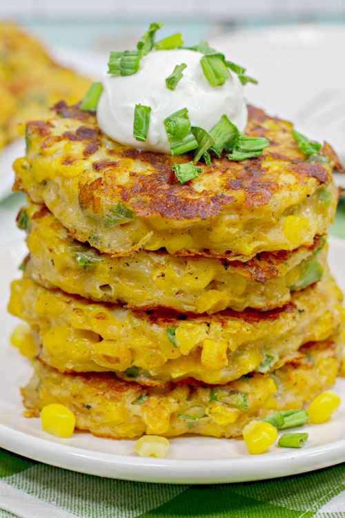 a stack of 4 corn fritters topped with sour cream and green onions.