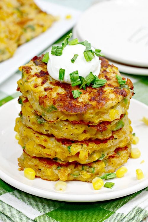 a stack of pan fried corn fritters garnished with sour cream and green onions.