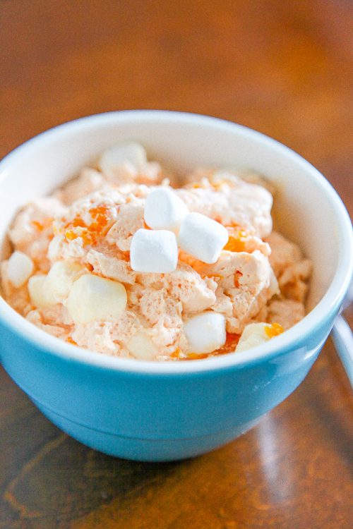 orange fluff salad topped with mini marshmallows in a blue ceramic bowl. 