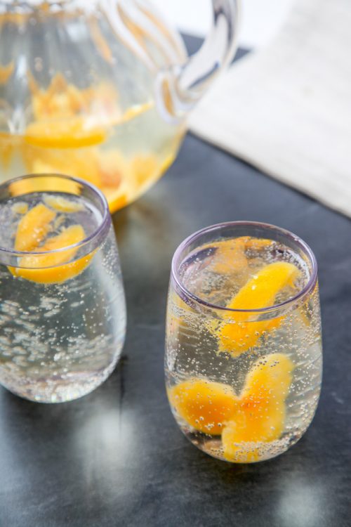 two clear glasses of white peach sangria on a black tabletop.