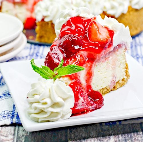 a slice of cheesecake topped with strawberries and served with whipped cream and mint.