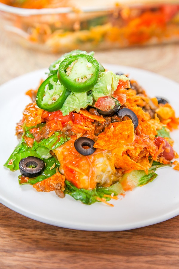dorito casserole on a white plate topped with lettuce, black olives, and jalapeno