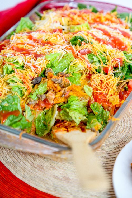casserole in a glass baking dish topped with cheese, lettuce, and Catalina dressing