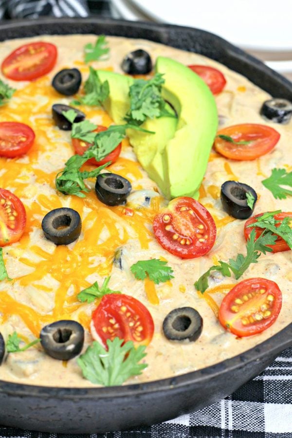 Warm bean dip topped with olives and tomatoes in a black skillet. 