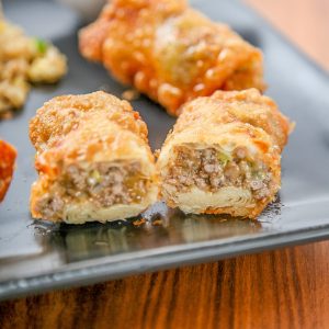 an eggroll filled with ground beef and cheese cut in half on a plate.
