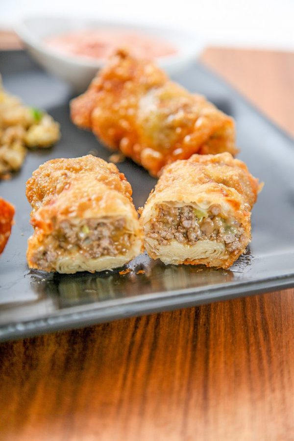 an eggroll filled with ground beef and cheese cut in half on a plate.