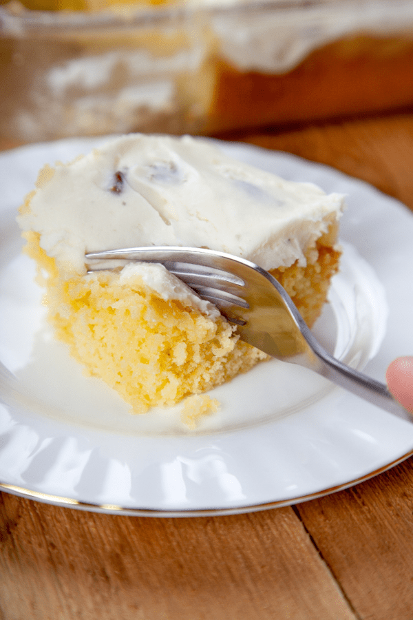 a fork cutting into a pineapple cake with cream cheese frosting.