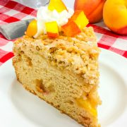 a slice of peach coffee cake topped with whipped cream on a white plate.