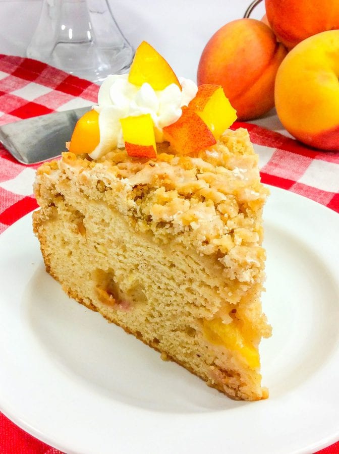 a slice of peach coffee cake topped with whipped cream on a white plate.