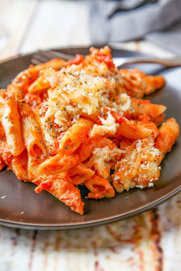 a black plate with penne pasta covered in cheese and sauce.