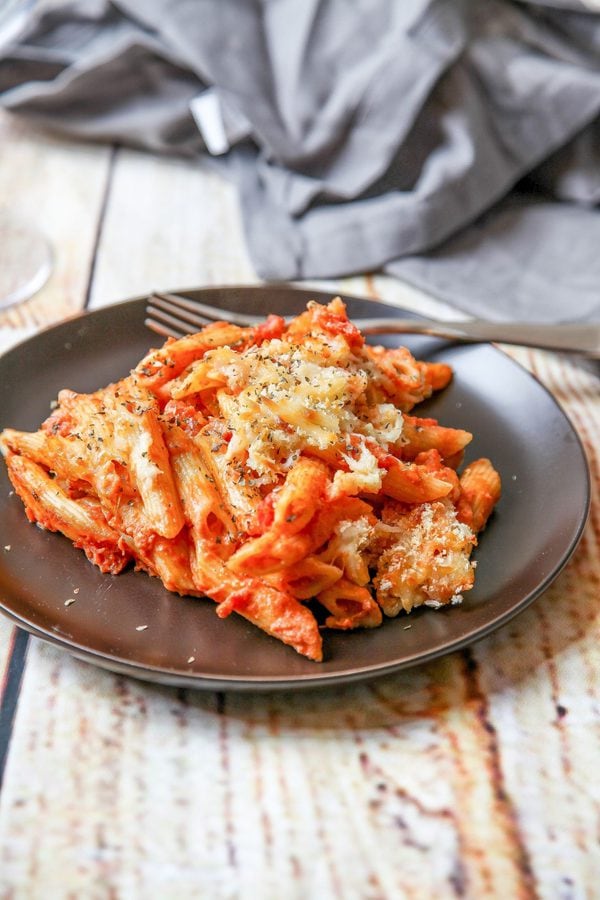 saucy pasta al forno on a black plate with a napkin in the background.
