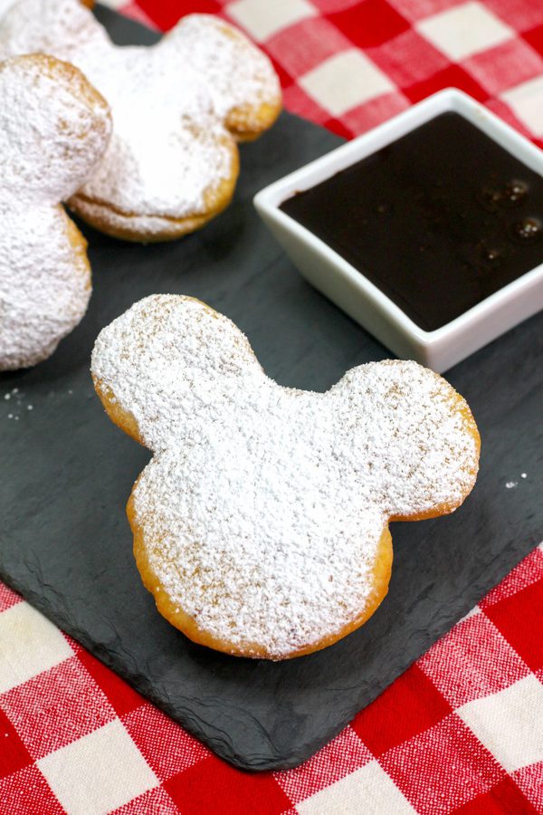 A mickey mouse shaped beignet on a black napkin.