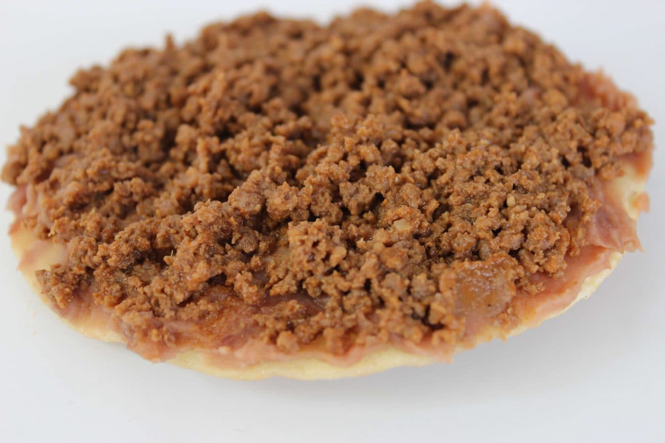 a fried tortilla topped with refried beans and seasoned ground beef. 