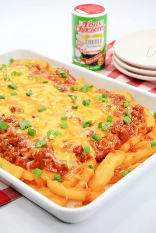 french fries topped with beefy chili, shredded cheese, and green onions in a white square dish. 