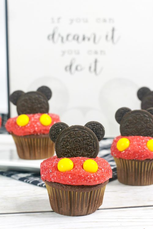 three mickey mouse cupcakes topped with red frosting and oreo cookies.