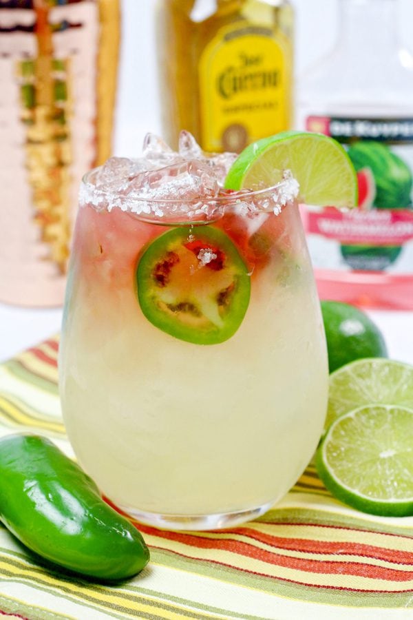 a jalapeno margarita with alcohol bottles and a cocktail shaker in the background.