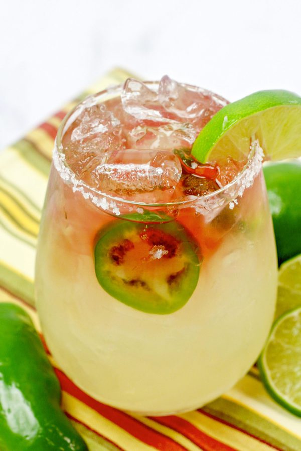 a texas margarita in a salted glass with jalapeno and garnished with a lime wedge.