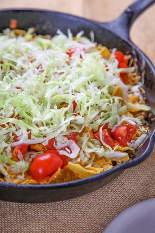 a cast iron skillet walking taco casserole topped with lettuce and tomato.