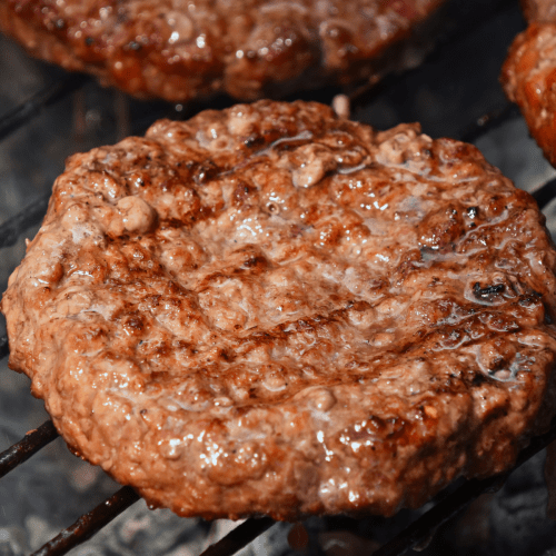 a juicy burger patty on the grill. 