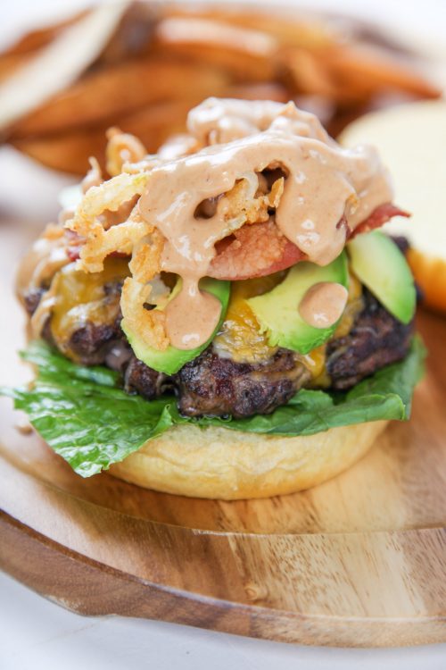 an openfaced cheeseburger piled high with bacon, avocado, onion strings, and creamy BBQ sauce.
