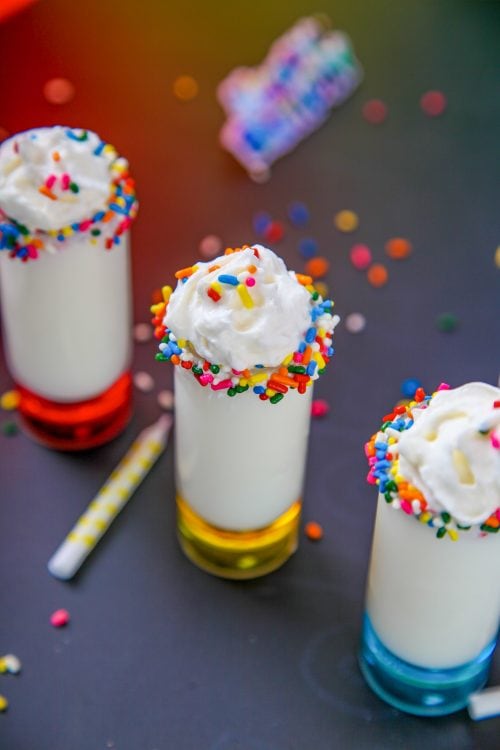 birthday cake shots in rainbow shot glassses with sprinkles and candles scatted around.