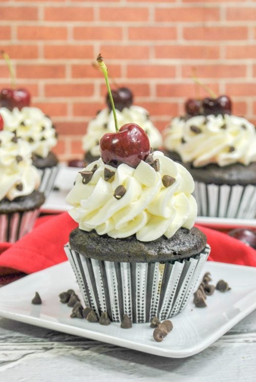 a black forest cupcake on a white plate with a brick wall in the background.
