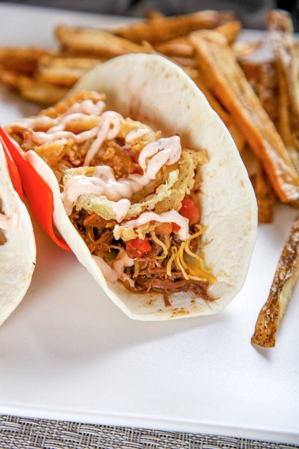 A brisket taco topped with cheese, fried onions, and a spicy sauce.